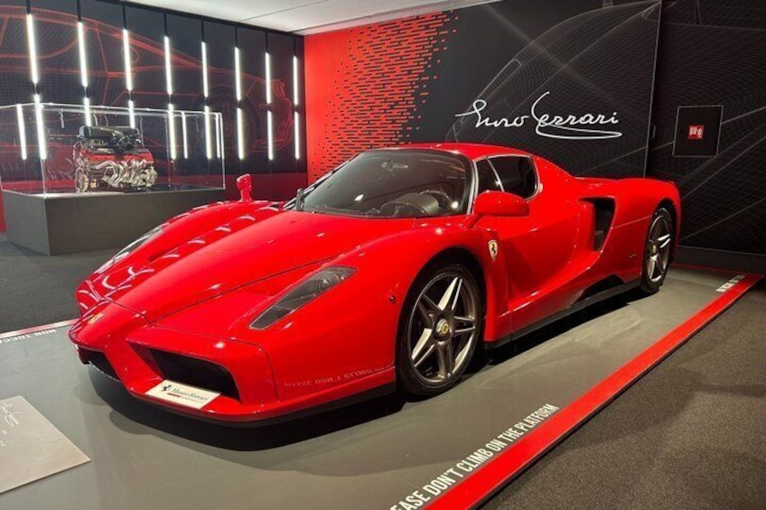 Een rode sportauto tentoongesteld, met een Ferrari-logo en een waarschuwingsbord op de vloer. 1