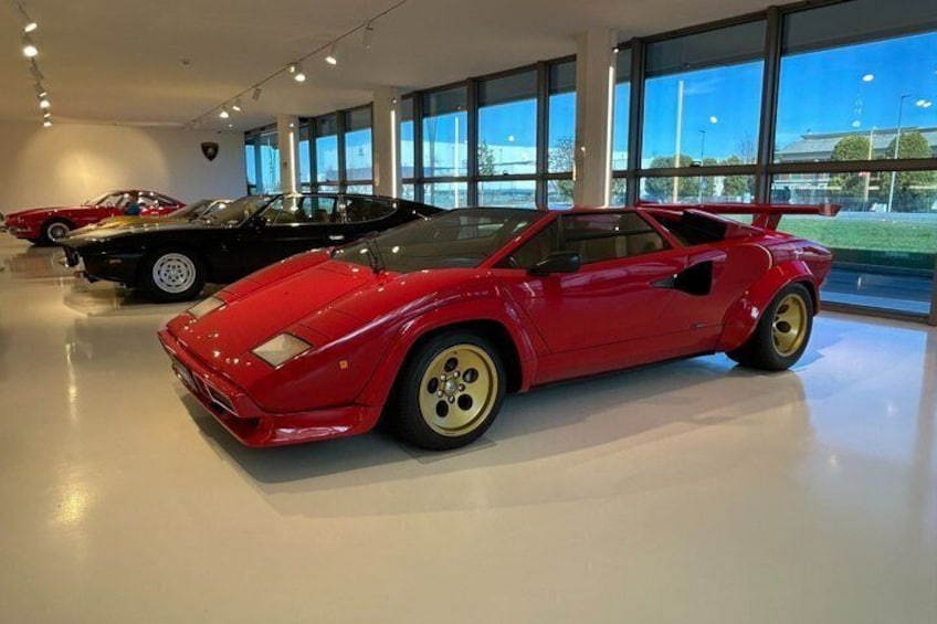 Een rode sportauto in een showroom met grote ramen en andere auto's op de achtergrond. 2