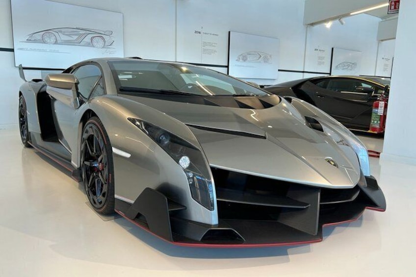 Een zilvergrijze sportauto met een laag profiel, zwarte achtervleugel en rode accenten in een showroom. 5
