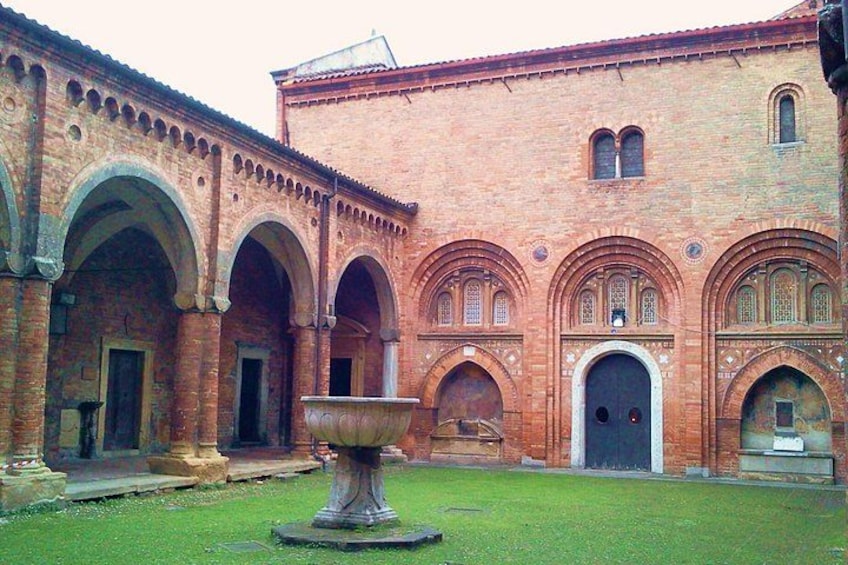 Un cortile con una grande fontana in pietra, passaggi ad arco e un edificio in mattoni con diverse finestre. 5
