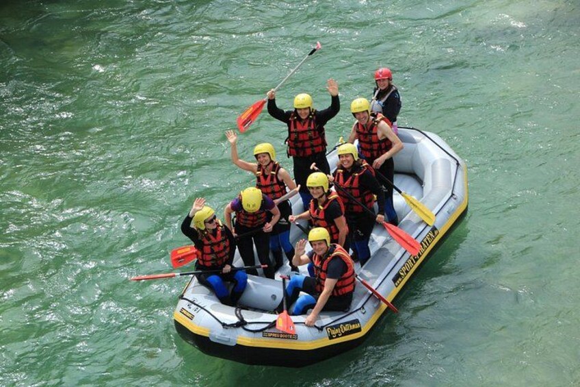 A group of people in a raft with paddles, wearing life jackets and helmets, on a body of water. 3