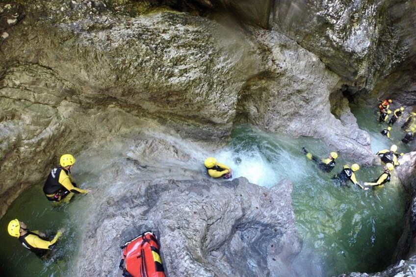 A group of people in yellow helmets navigating a narrow water channel in a rocky cave. 4