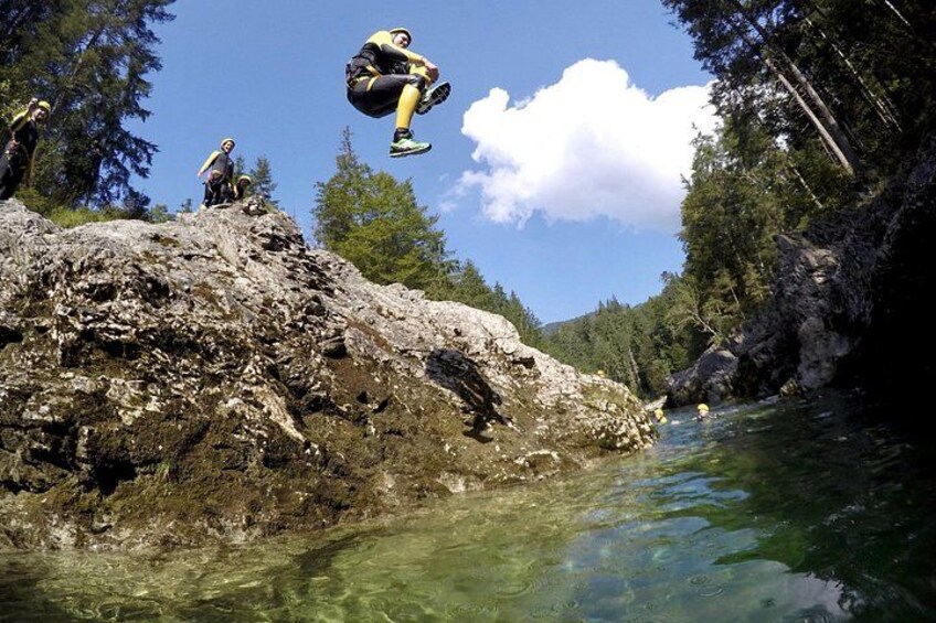 A person jumping off a rocky cliff into a river surrounded by trees. 1