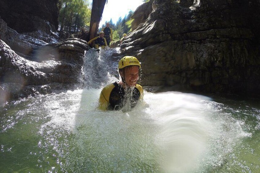 A person in a yellow helmet and wetsuit swimming in a river with a rocky background. 3