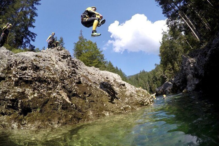 A person jumping off a rocky cliff into a river surrounded by trees. 1