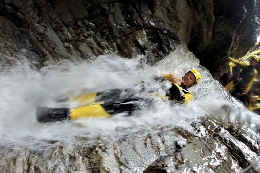 A person in a yellow helmet and life jacket navigating a white water rapids in a rocky canyon. 5