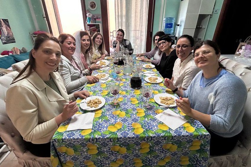 Un grupo de personas sentadas alrededor de una mesa con mantel floral, platos de comida y vasos de bebida. 2