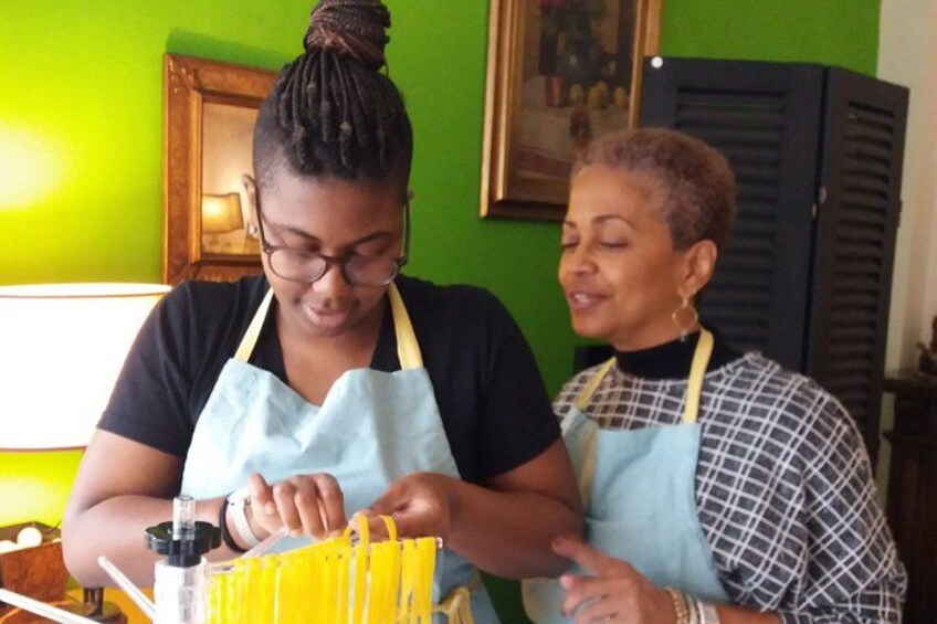 Dos personas con delantales, una sosteniendo un recipiente amarillo, en una habitación con paredes verdes y un cuadro enmarcado. 2