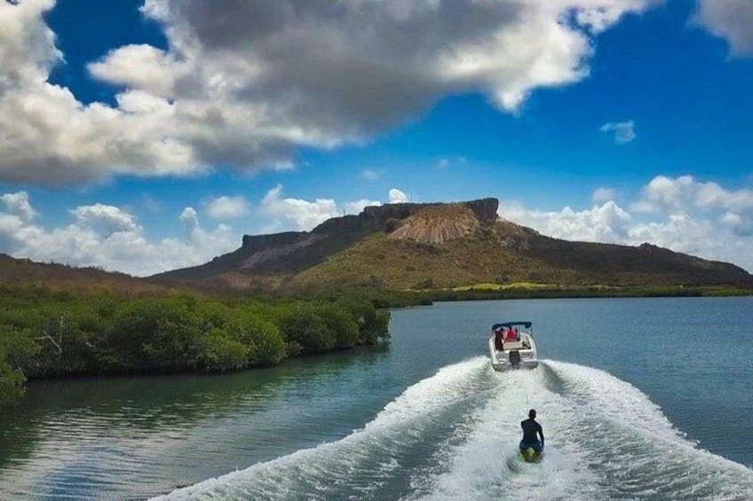 A person wakeboarding behind a boat on a calm lake with mountains in the background. 4