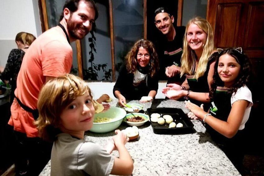 A group of people sitting around a kitchen table with food and a baking tray. 2