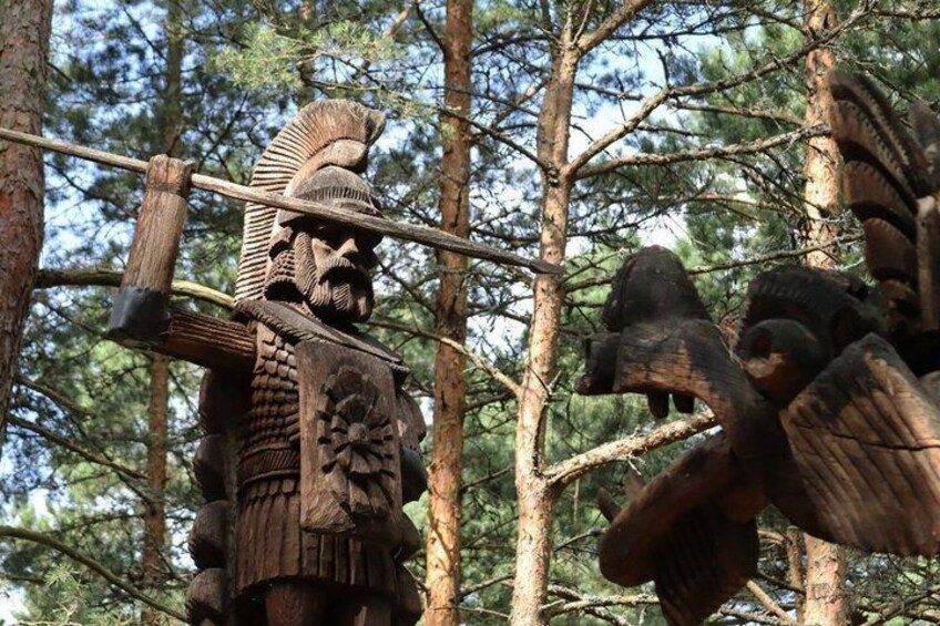 A wooden sculpture of a warrior with a spear, surrounded by trees. 1