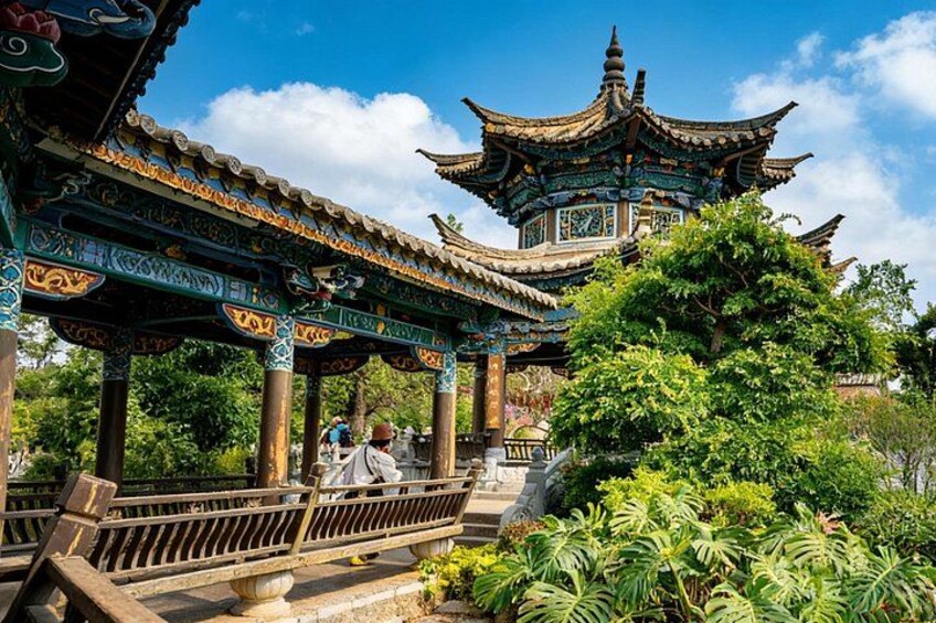 A traditional Chinese pavilion with ornate roof and columns, surrounded by lush greenery and a clear blue sky. 2