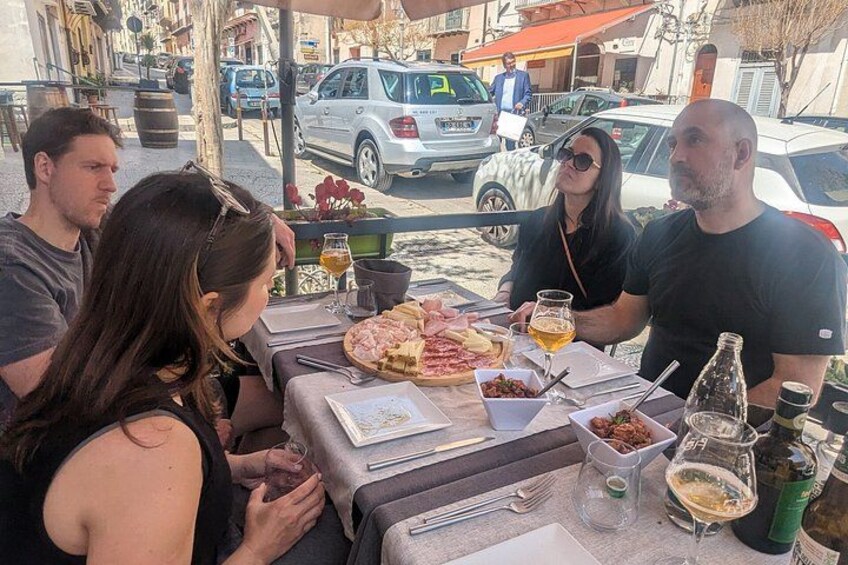 Eine Gruppe von Menschen speist im Freien an einem Tisch mit Essen und Getränken. 4