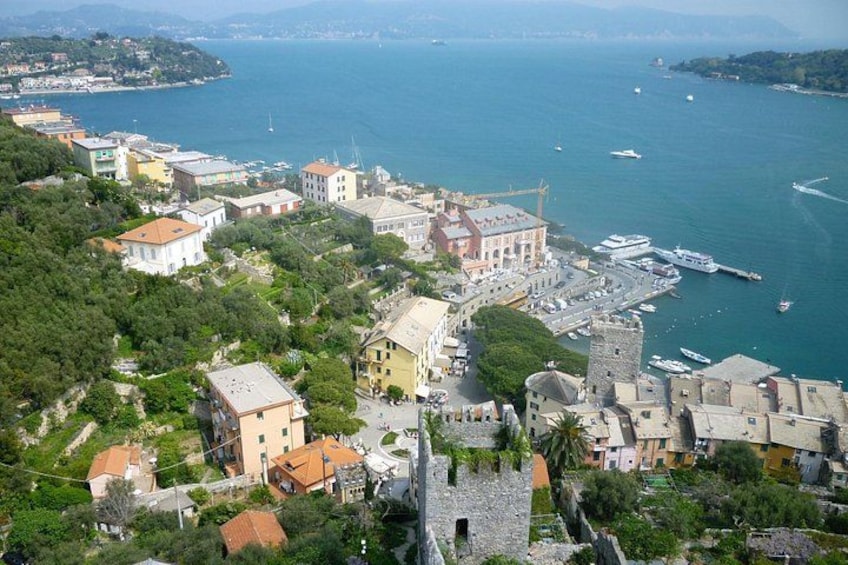 A coastal town with historic buildings, a marina, and a mountainous backdrop. 1