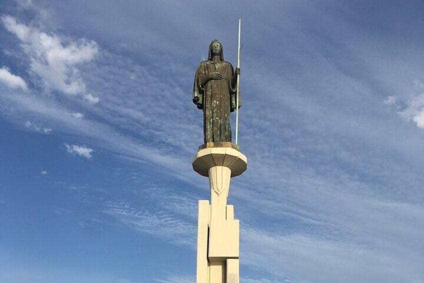 Eine Statue einer Person mit Speer, auf einem Sockel befestigt, vor blauem Himmel. 3
