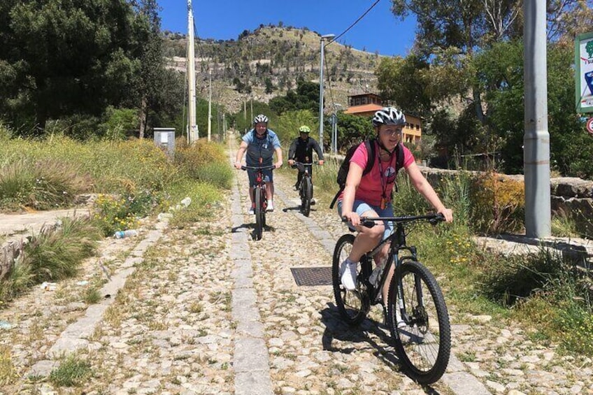 Radfahrer auf einem Kopfsteinpflasterweg mit hügeliger Landschaft im Hintergrund. 1