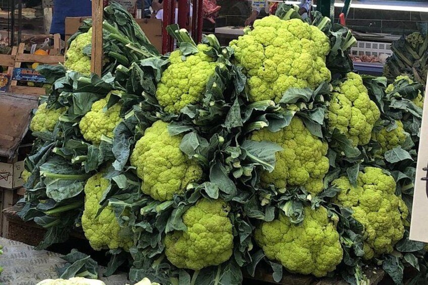 A large pile of green cauliflower heads with dark green leaves. 3