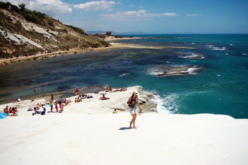 Une plage où des gens se prélassent au soleil, un rivage rocheux et l’océan. 1