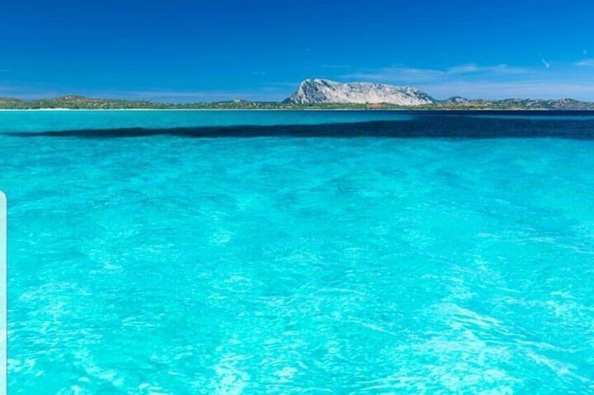 A clear turquoise sea with a rocky island in the distance. 5