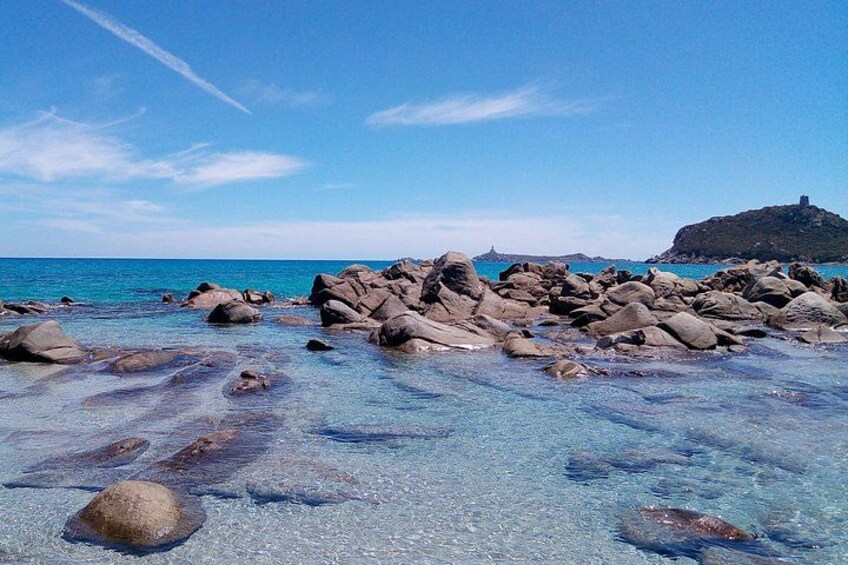 A rocky beach with clear water and a distant hill. 1