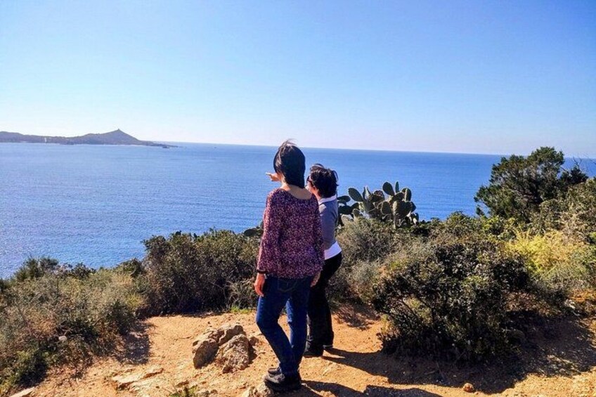 Dos personas están de pie en un sendero de tierra con vistas a un paisaje costero, con una vista despejada del mar y una montaña distante. 4
