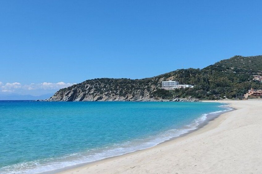 Una playa con agua turquesa cristalina, una orilla arenosa y una colina con edificios al fondo. 3