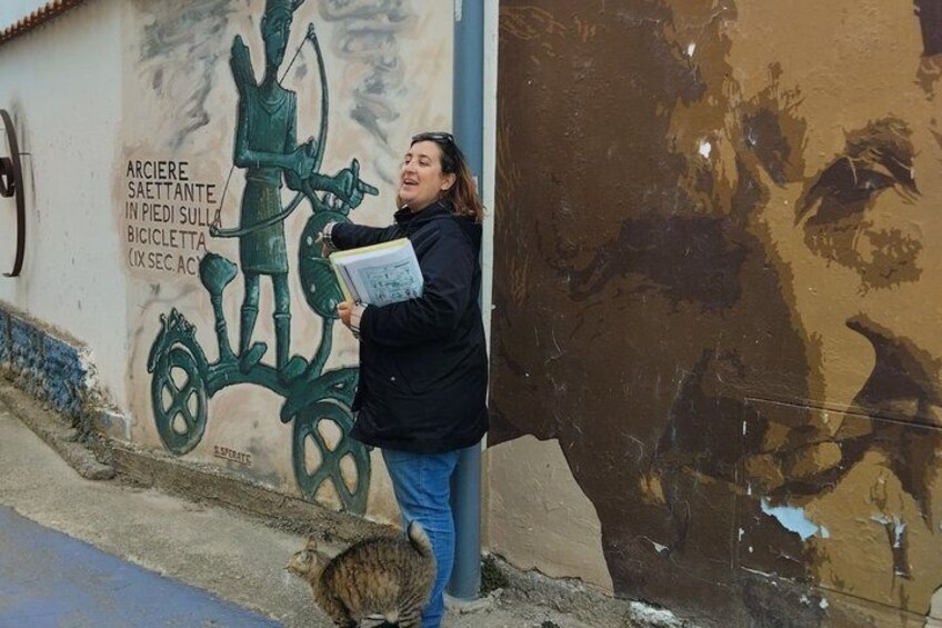 A person leaning against a wall with a mural of a figure on a bicycle. 2