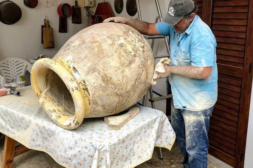 A person cleaning a large ceramic pot on a table with a floral tablecloth. 3