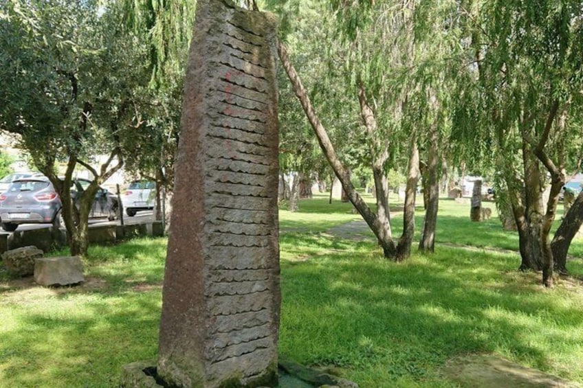 A stone pillar in a park with trees and parked cars in the background. 3