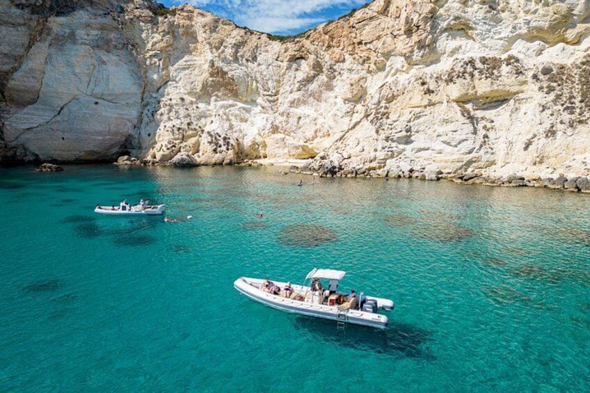 Ein Boot auf türkisblauem Wasser, im Hintergrund felsige Klippen. 1