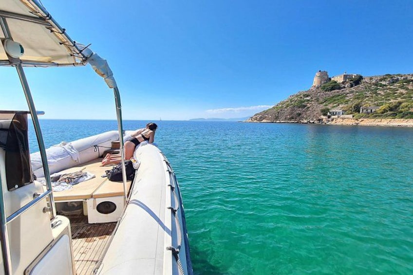 Ein Boot auf ruhigem türkisblauem Wasser, eine Person entspannt sich auf dem Deck, und im Hintergrund ein historisches Gebäude auf einem Hügel. 4