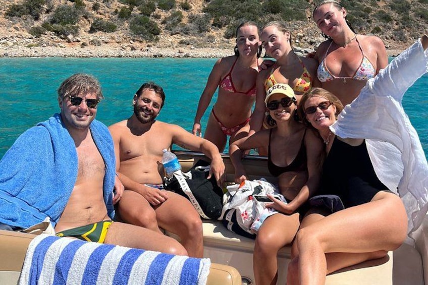 Eine Gruppe von Menschen auf einem Boot in der Nähe eines türkisfarbenen Meeres, im Hintergrund felsiges Gelände. 5