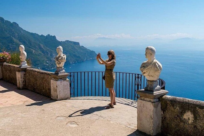 A woman taking a photo, overlooking a coastal landscape with statues and a clear sky. 3