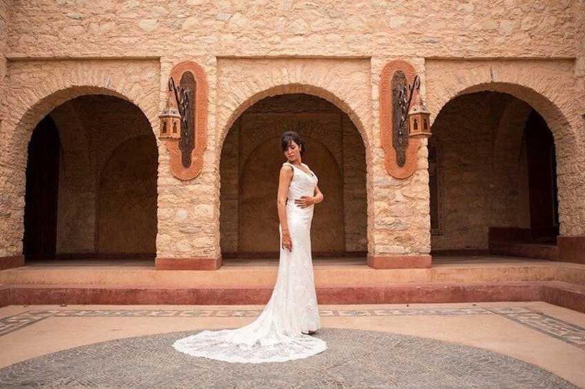 A person in a white dress standing in front of a stone building with arches and lanterns. 1