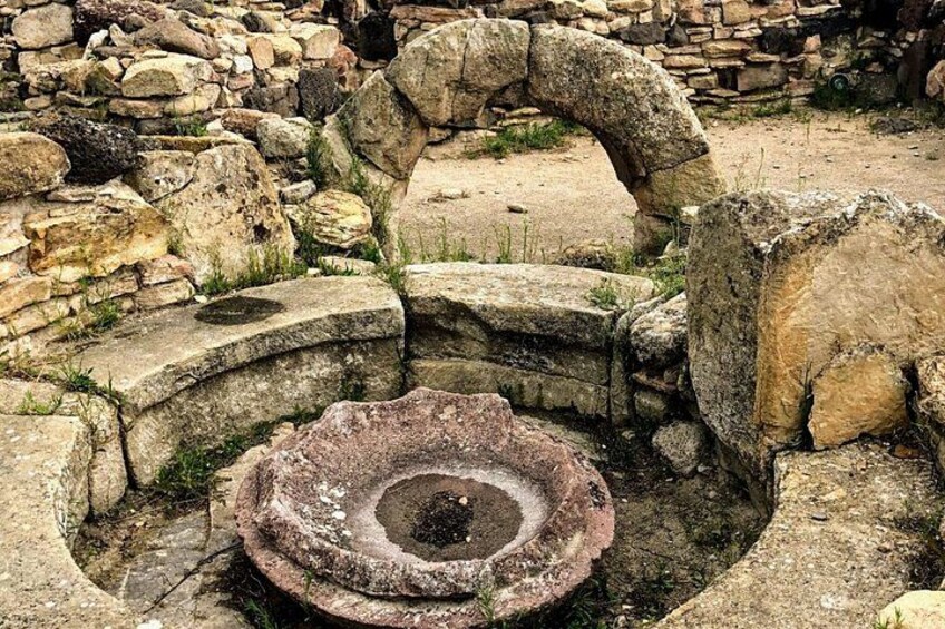 Ancient stone ruins with a circular stone structure and an arched stone formation. 4