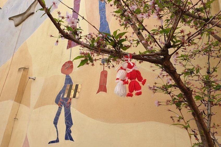 A mural with a figure holding a book, a hanging lantern, and a tree with pink blossoms. 1