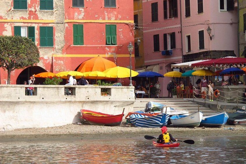 A waterfront with colorful boats, a person kayaking, and buildings with outdoor seating. 1