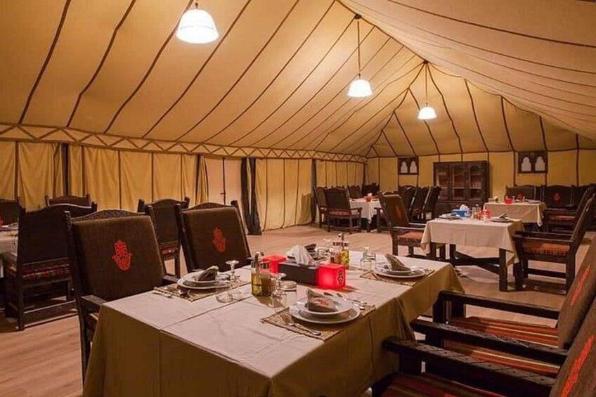 An indoor dining area with tables set for a meal, tents, and hanging lights. 1