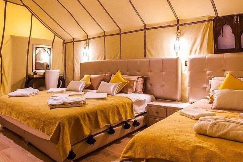 A tented room with two beds, each with a yellow bedspread and pillows, and a nightstand with a lamp. 4