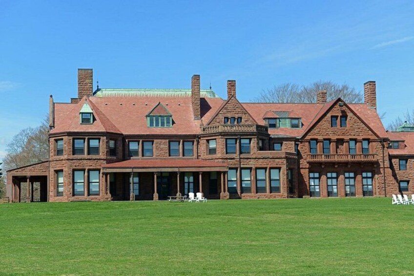 A large brick building with multiple chimneys, a green lawn, and a clear blue sky. 3