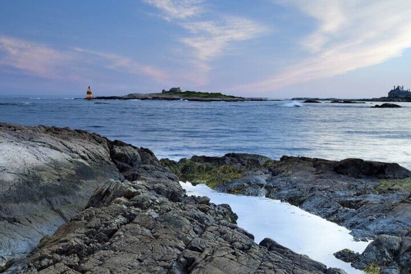 A rocky shoreline with a lighthouse in the distance and a building on a small island. 5