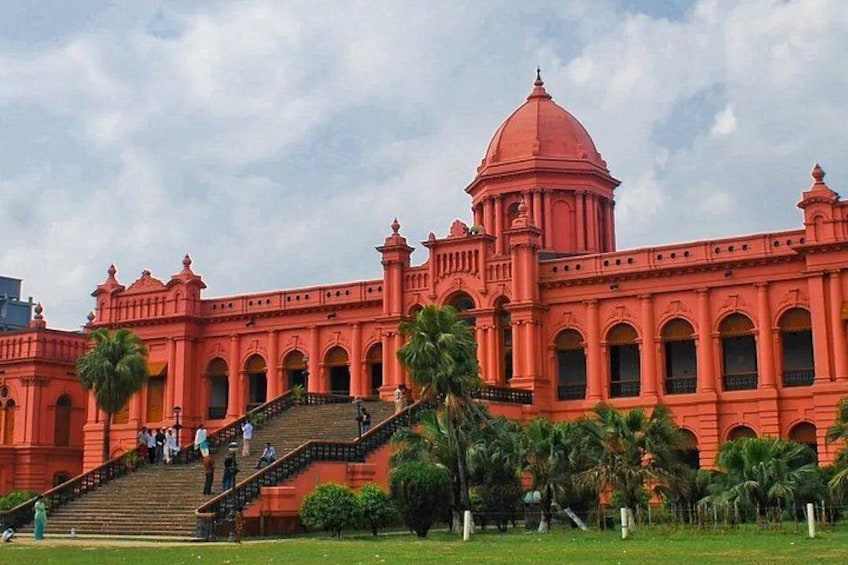 A large, red colonial-style building with a dome and arched windows, surrounded by palm trees and a staircase leading up to the entrance. 3