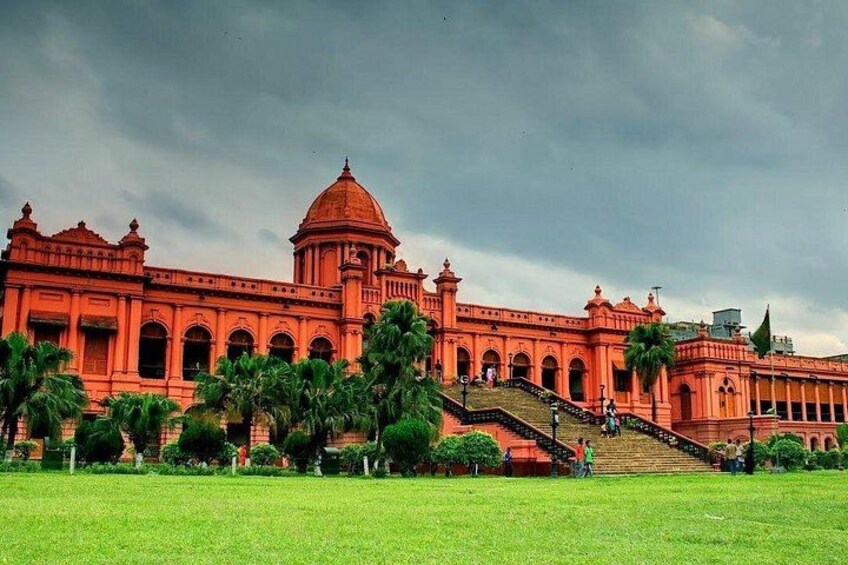 A large red building with a dome and arched windows, surrounded by a green lawn and palm trees. 4