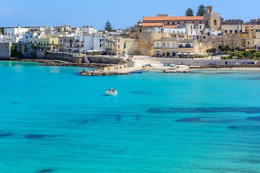 A coastal town with buildings, a clear blue sea, and a small boat. 1