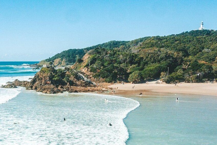 Une plage avec des vagues, un phare et une colline plantée d’arbres. 1