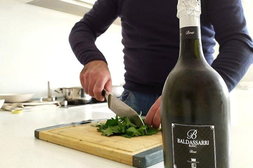 Una persona che taglia verdure su un tagliere di legno, una bottiglia di vino Balthazar e un piano di lavoro in cucina. 5