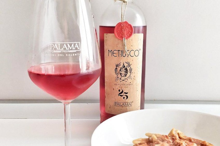 Un bicchiere di vino rosso, una bottiglia di vino Metilusco e un piatto di pasta. 4
