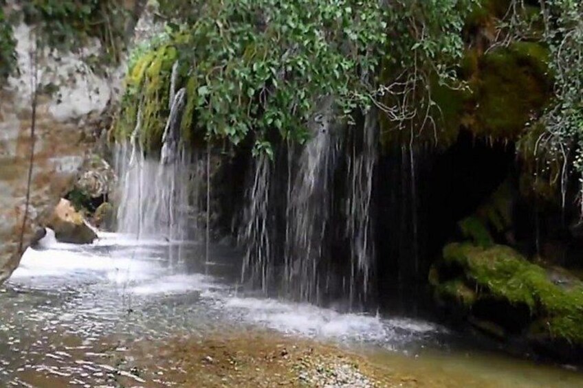 A waterfall cascading over moss-covered rocks into a shallow pool. 2