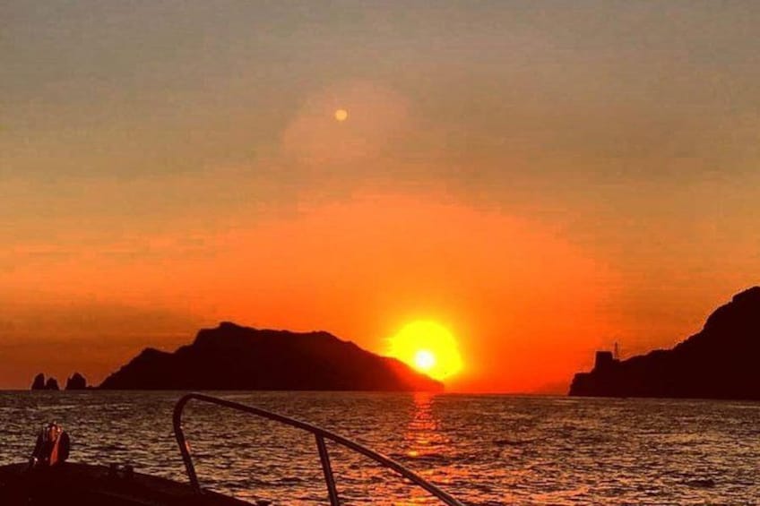 Un coucher de soleil sur l’eau, avec les silhouettes de montagnes et une rambarde en arrière-plan. 5