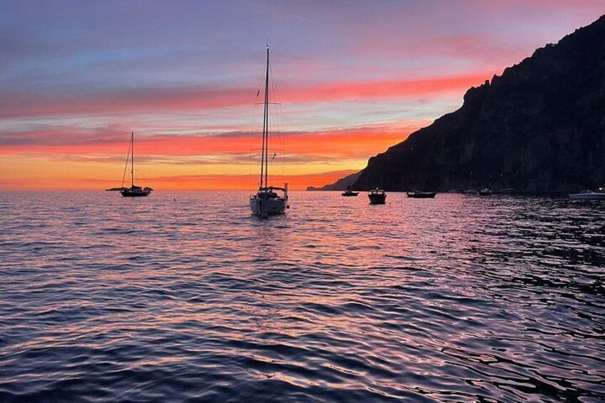 Un coucher de soleil sur une mer calme, avec des voiliers ancrés près d’une côte rocheuse. 3